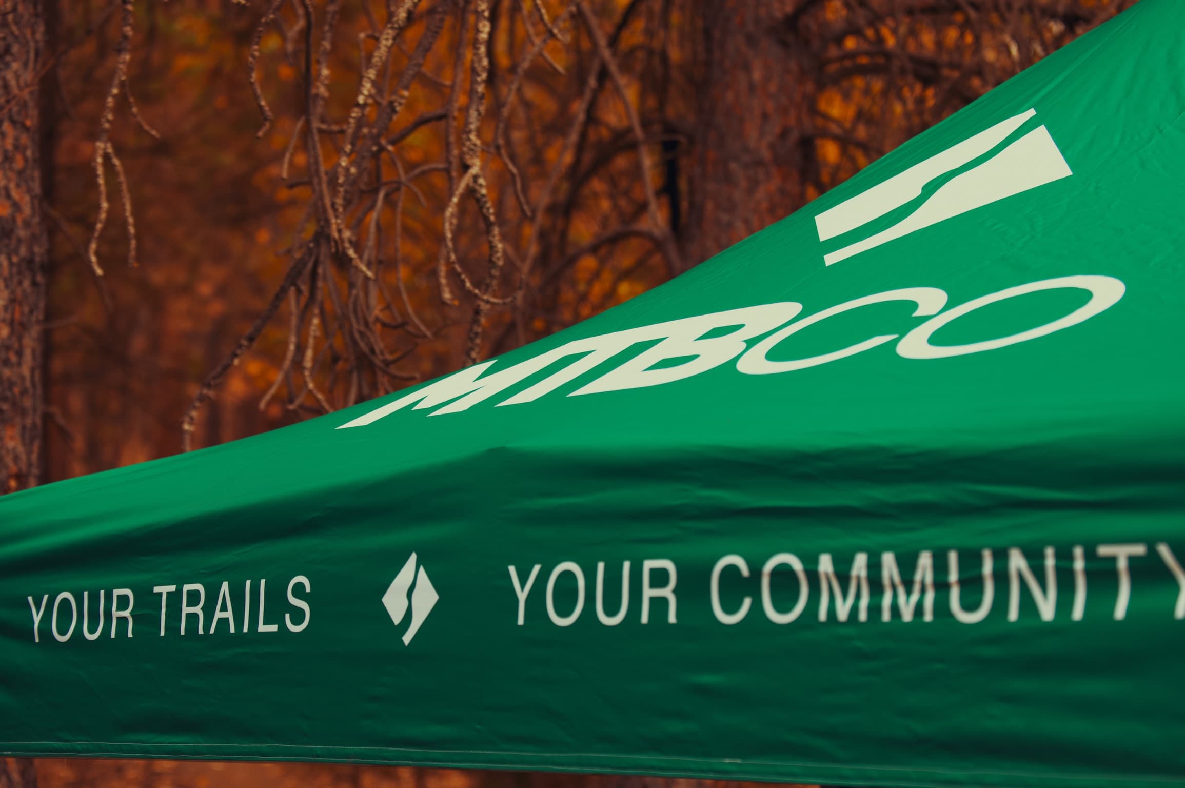 MTBCO branded event tent in autumn forest, reading "your trails, your community"